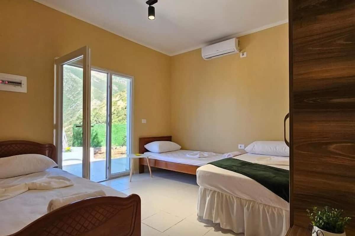 A room with two beds, a sliding glass door to a balcony, and a ceiling-mounted light fixture.