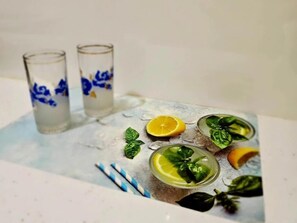 A glass table with two glasses and a bowl containing a beverage with lemon and basil. - Lemon House Borsh (Lukovë)