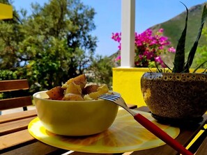 A bowl of food on a yellow placemat with a fork, a potted plant, and a wooden bench. - Lemon House Borsh (Lukovë)
