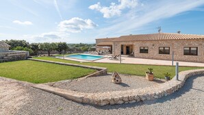 Un edificio de piedra con piscina, mobiliario exterior y un césped bien cuidado.