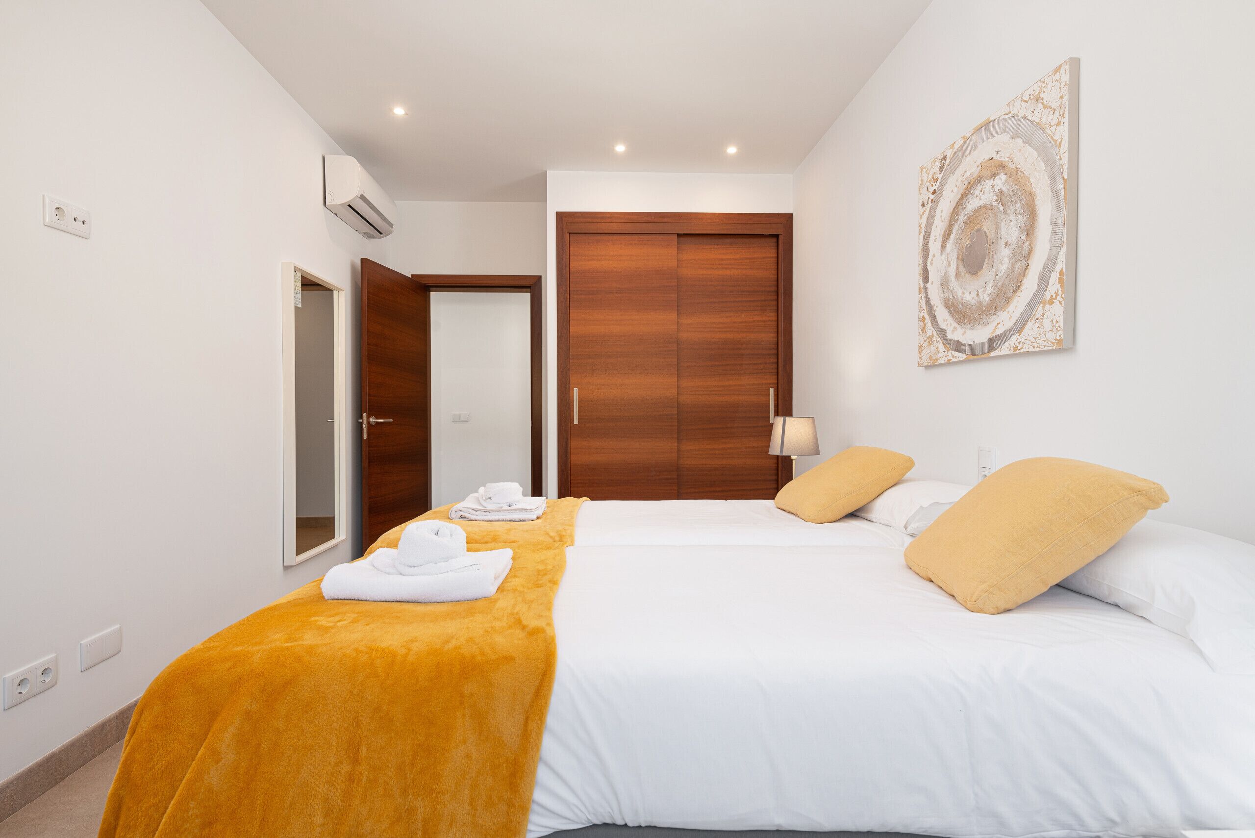 Una camera d'albergo con un letto, un armadio in legno, un'opera d'arte appesa al muro e un bagno visibile attraverso una porta aperta.
