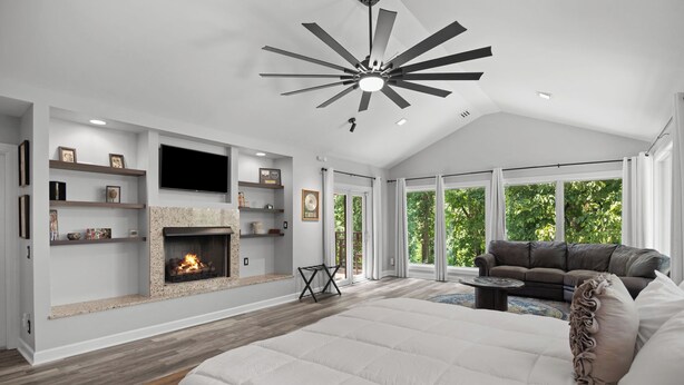 A spacious bedroom with a large bed, a fireplace, a ceiling fan, and a view of the outdoors.