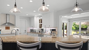 A modern kitchen with white cabinets, granite countertops, and pendant lighting.