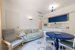 A compact living space with a sofa, a dining table, a chair, a kitchenette, and a ceiling light fixture. - La Favola di San Martino (Naples)