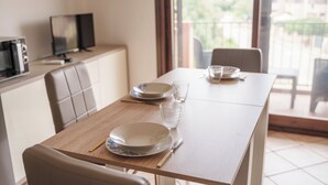 Una mesa de comedor con platos, vasos y cubiertos. Un televisor está sobre un mueble a la izquierda.