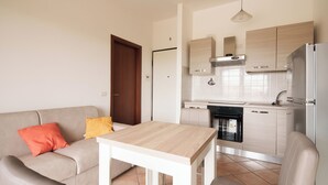 Un espacio habitable compacto con kitchenette, un sofá con cojines y una pequeña mesa de comedor.