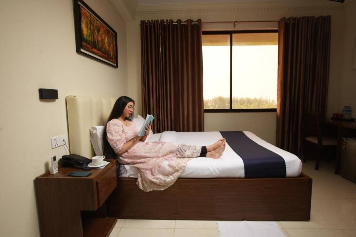 A room with a bed, a desk, a chair, a painting on the wall, and a window with curtains.