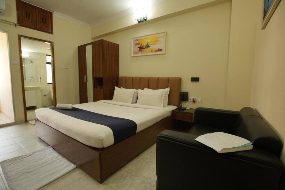 A bedroom with a bed, a nightstand, a black leather chair, and a painting on the wall.
