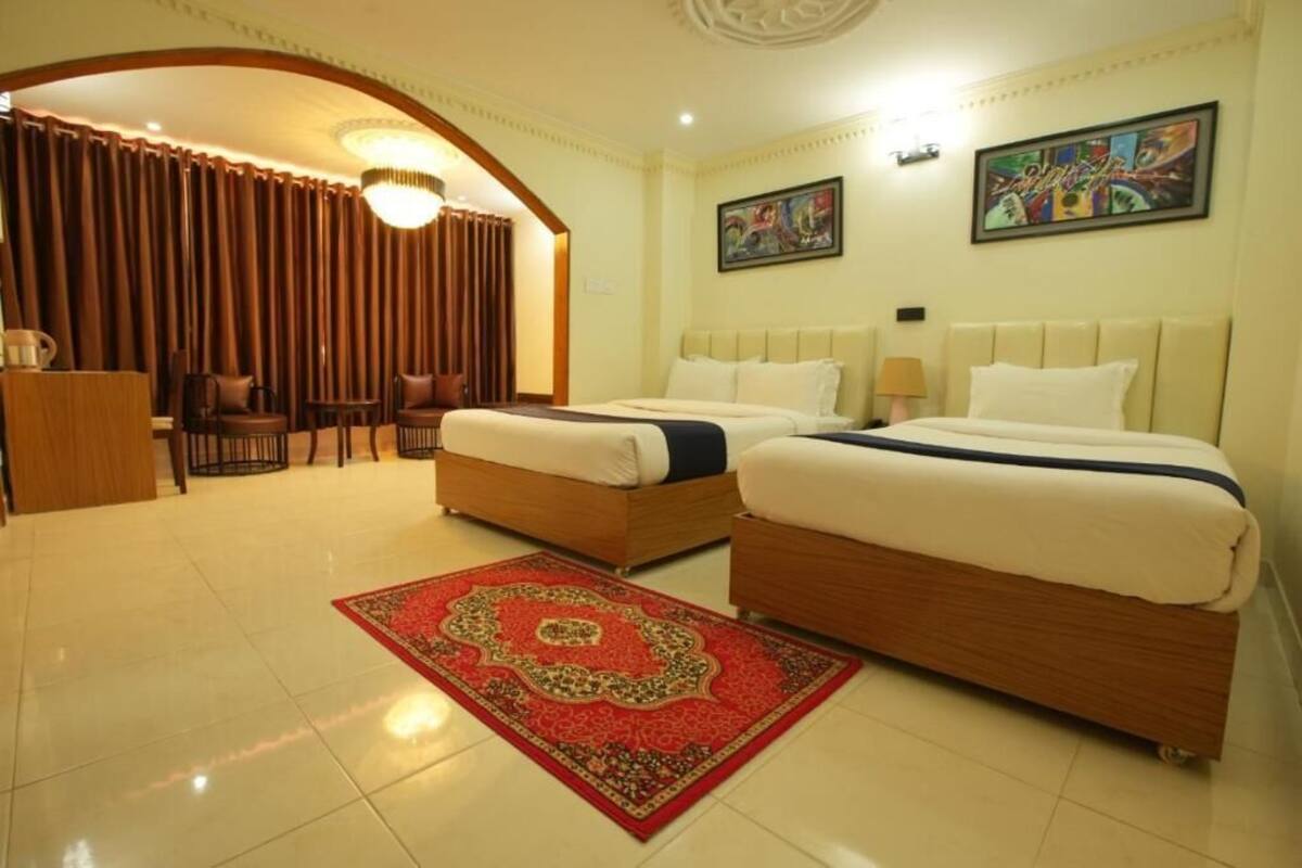 A hotel room with two beds, a red carpet, a desk, and a chair.