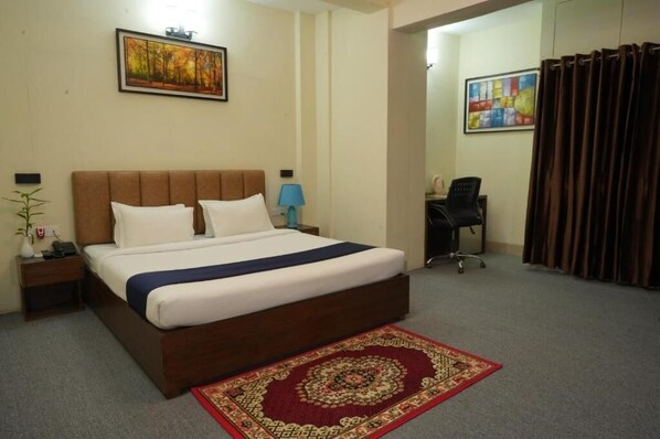 A hotel room with a large bed, a desk, a chair, a nightstand, a lamp, and a painting on the wall.