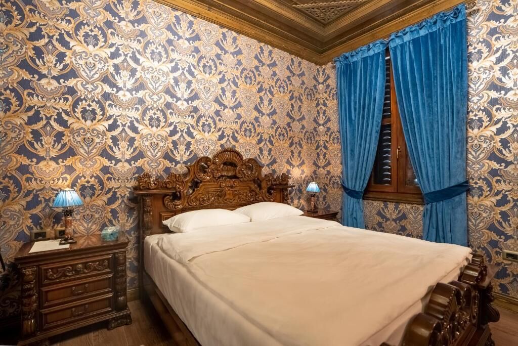 A bedroom with a large bed, ornate wooden headboard, and blue curtains.