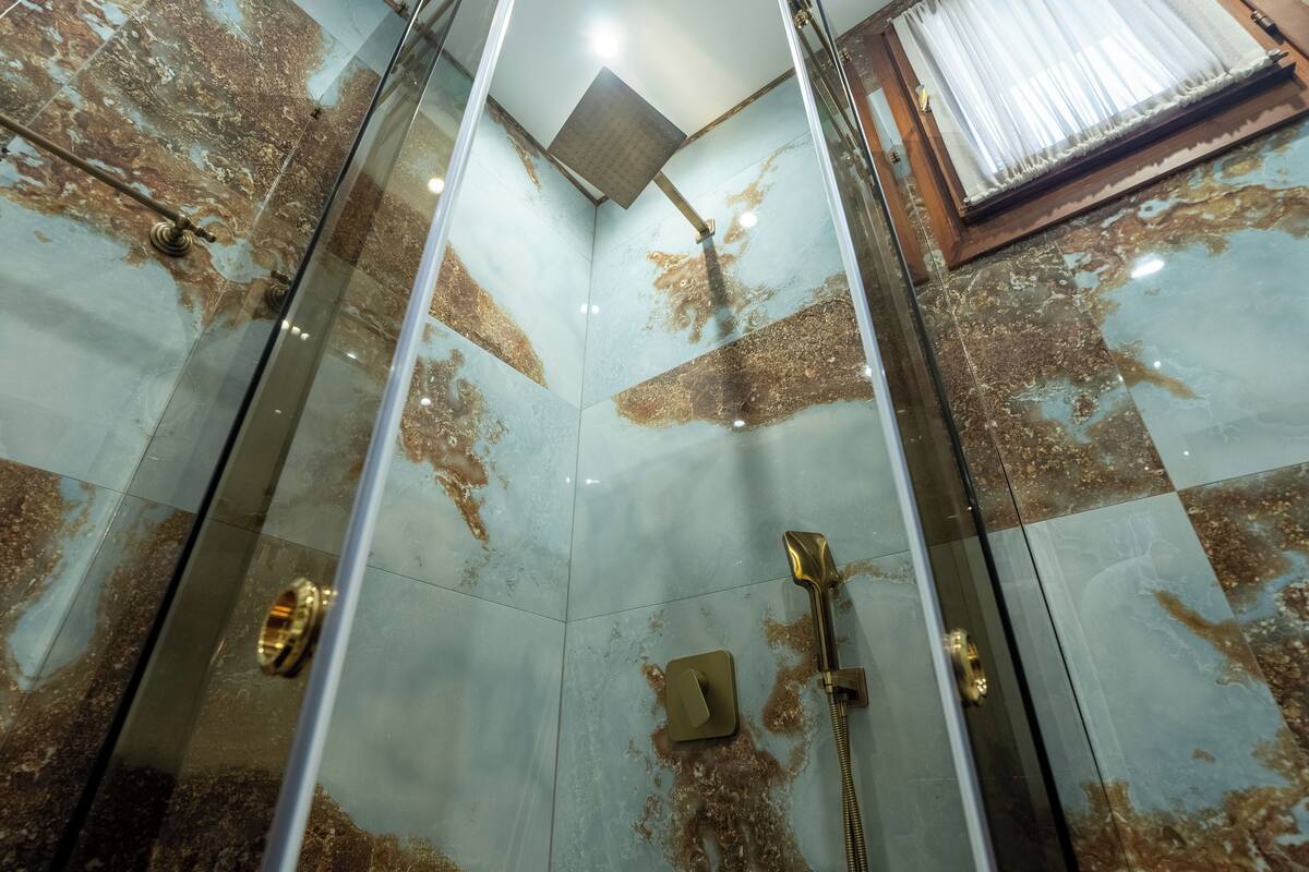 Une douche avec des parois en verre, un pommeau de douche à main et un pommeau de douche fixé au mur.
