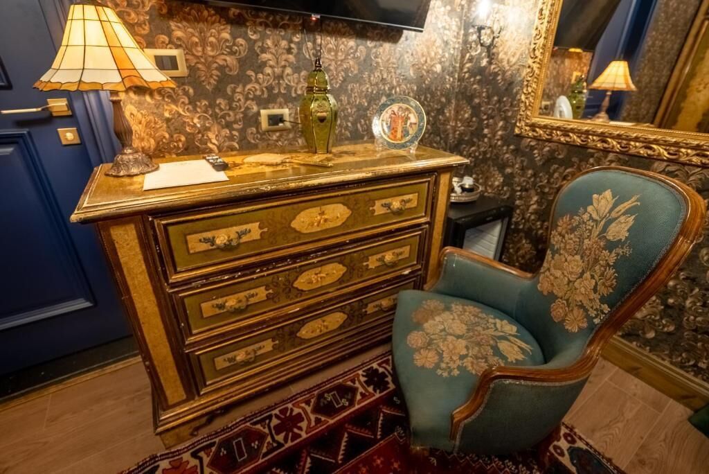 A room with a vintage-style dresser, a blue armchair with floral upholstery, and a patterned rug.