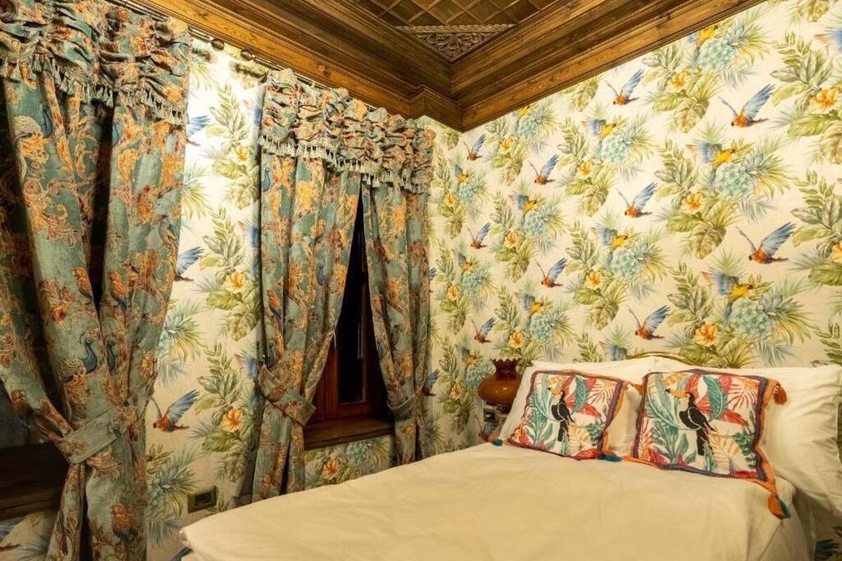 Une chambre avec un papier peint à motifs floraux, un lit avec des coussins assortis et des rideaux à imprimé tropical.