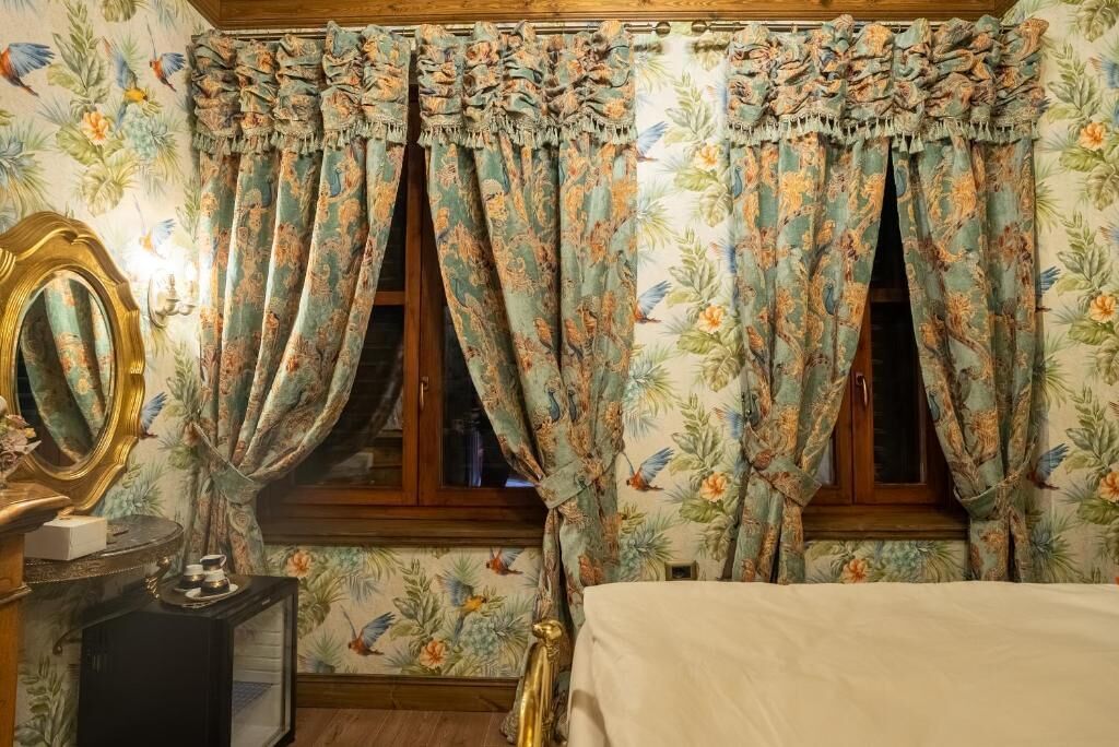 A room with floral wallpaper, a bed, a dresser with a mirror, and curtains with a tropical print.