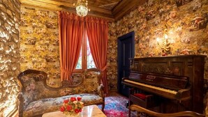 Une pièce avec un piano, un canapé, une table ornée d’un vase de fleurs et une fenêtre avec des rideaux.