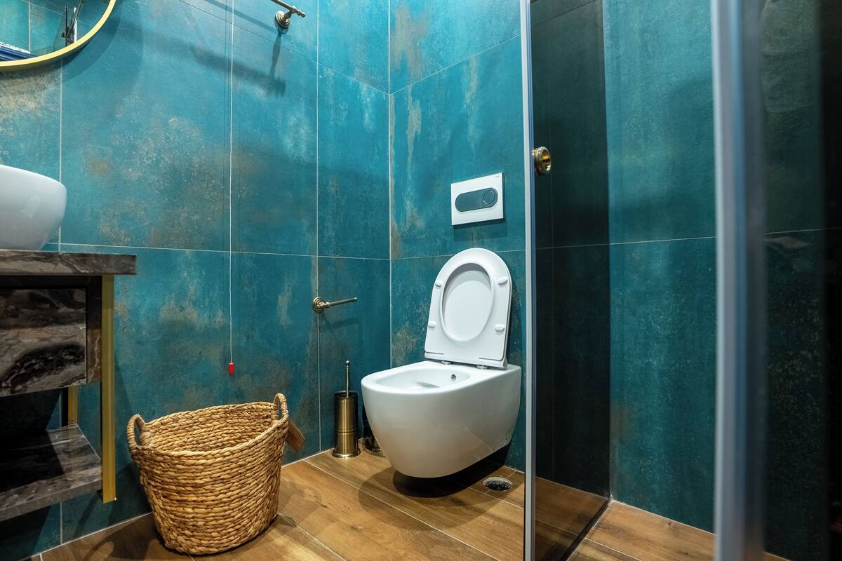 Une salle de bain au design moderne, avec des toilettes blanches, un plancher en bois et des murs de couleur turquoise.
