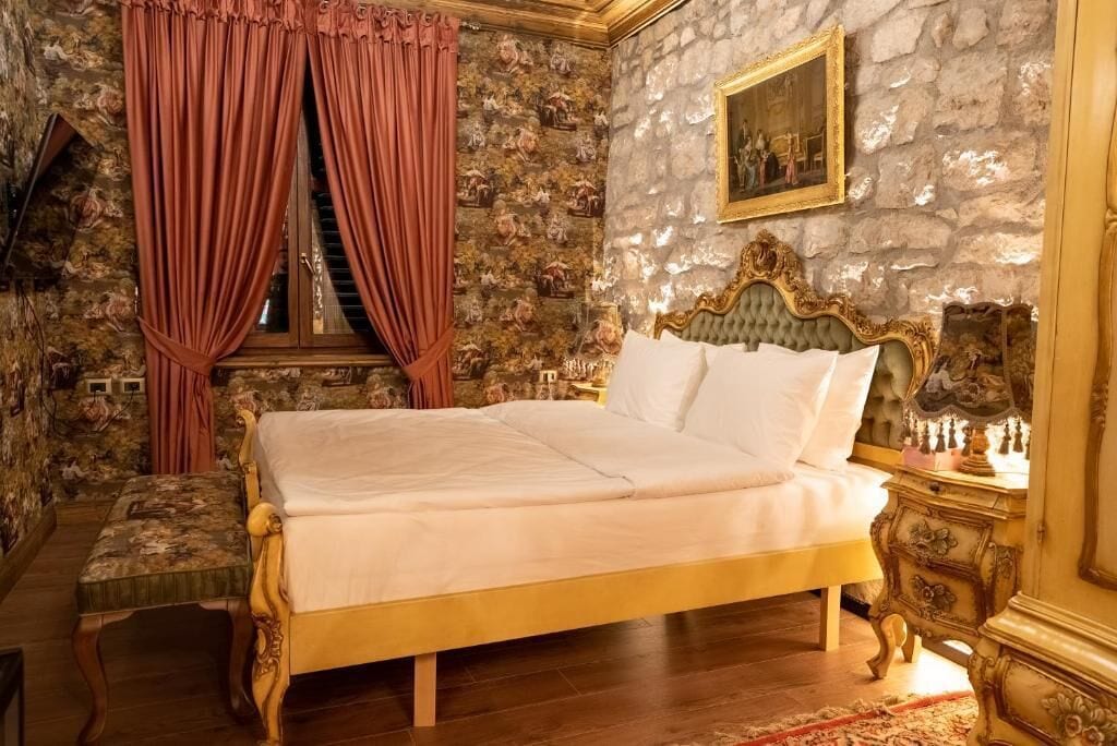 Une chambre avec un grand lit, une chaise en bois, un mur en pierre et un tableau.