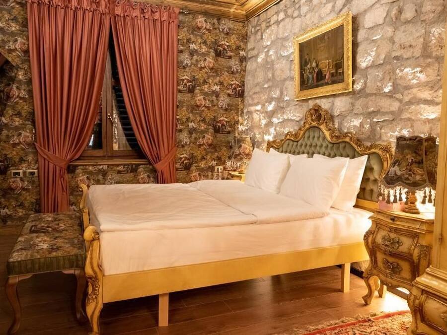 Une chambre avec un grand lit, une chaise en bois, un mur en pierre et un tableau.
