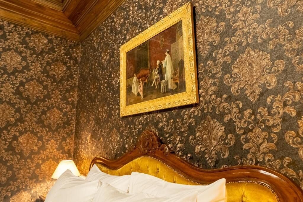 Una habitación con papel tapiz decorativo, una cama con cabecera de madera y un cuadro enmarcado en la pared.