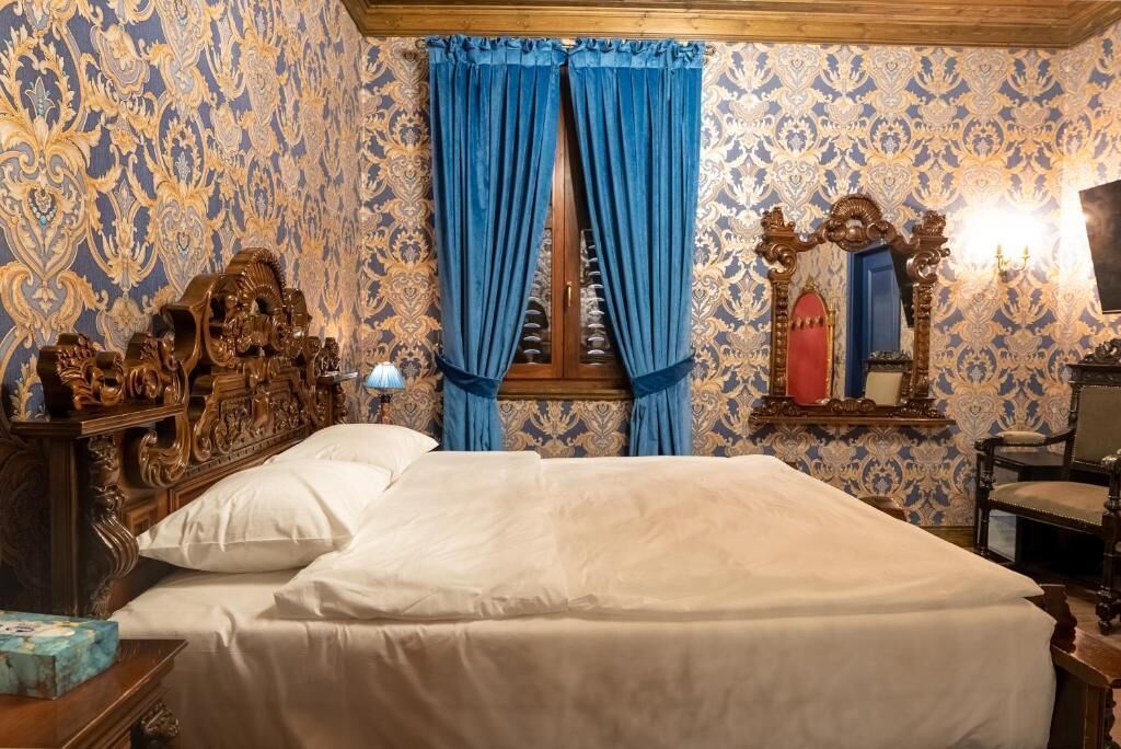 A room with a large bed, ornate wooden headboard, blue curtains, and a decorative mirror.