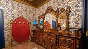 Une chambre luxueuse avec un papier peint décoratif, une tête de lit rouge et une commode en bois agrémentée de détails dorés.