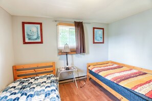 Een slaapkamer met twee houten bedden, een klein tafeltje met een lamp, en twee ingekaderde foto's aan de muur.