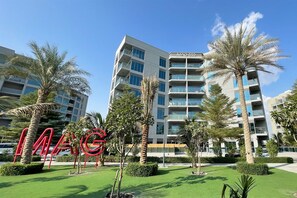A multi-story hotel with a modern design, featuring balconies and a well-maintained outdoor area with palm trees and manicured lawns.