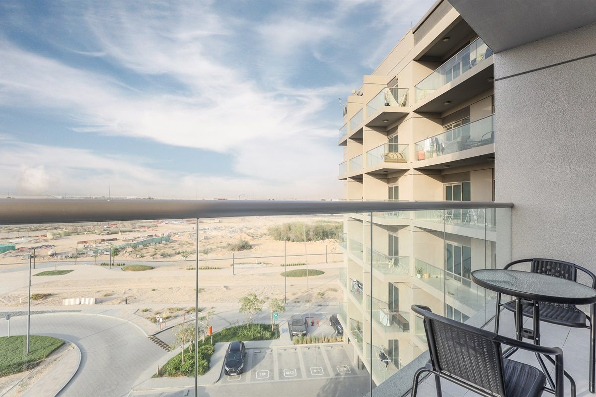 Un bâtiment moderne doté d’un balcon en verre donnant sur un paysage désertique.