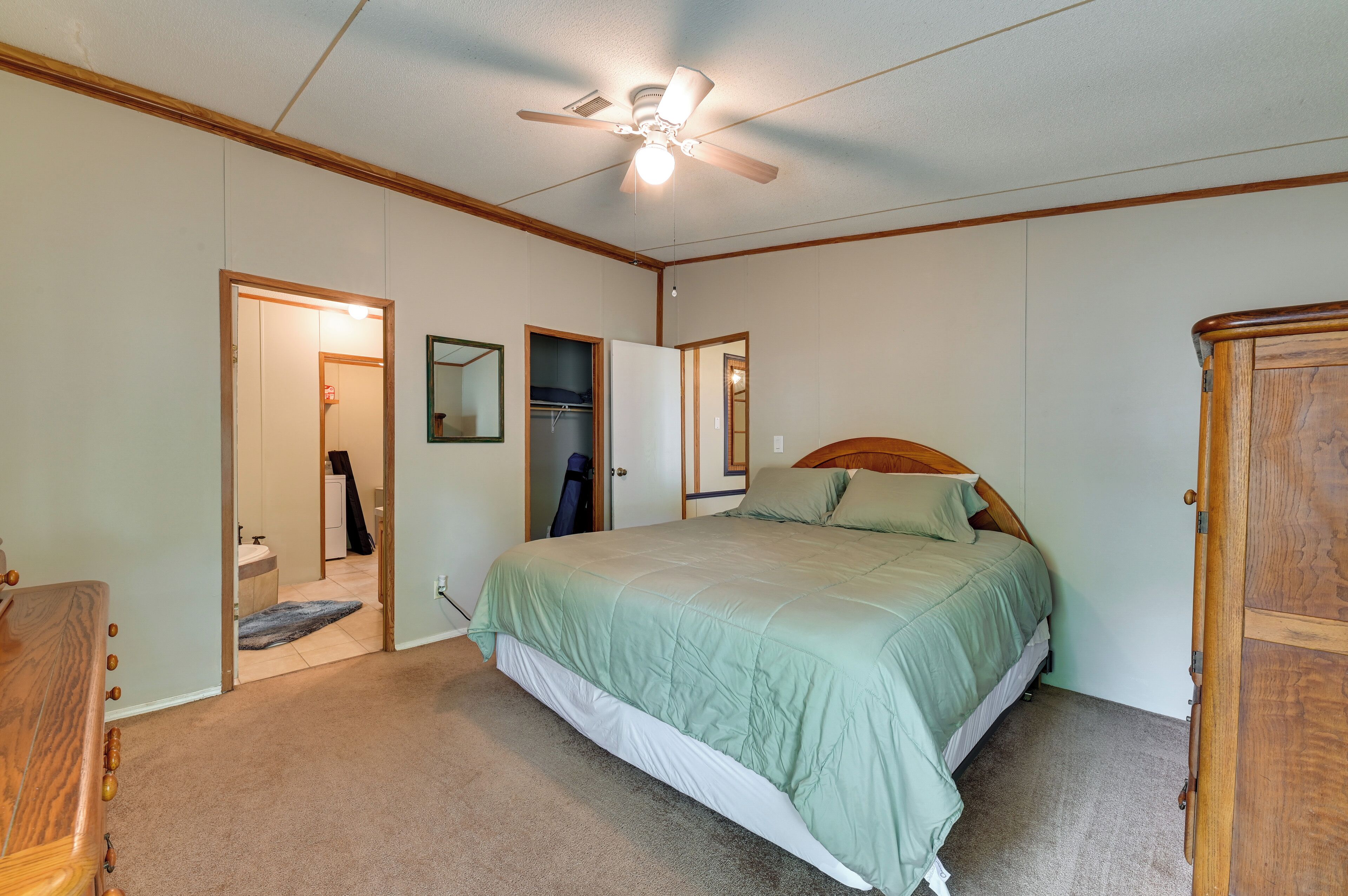 A bedroom with a bed, a ceiling fan, a wardrobe, and a bathroom visible through an open door.