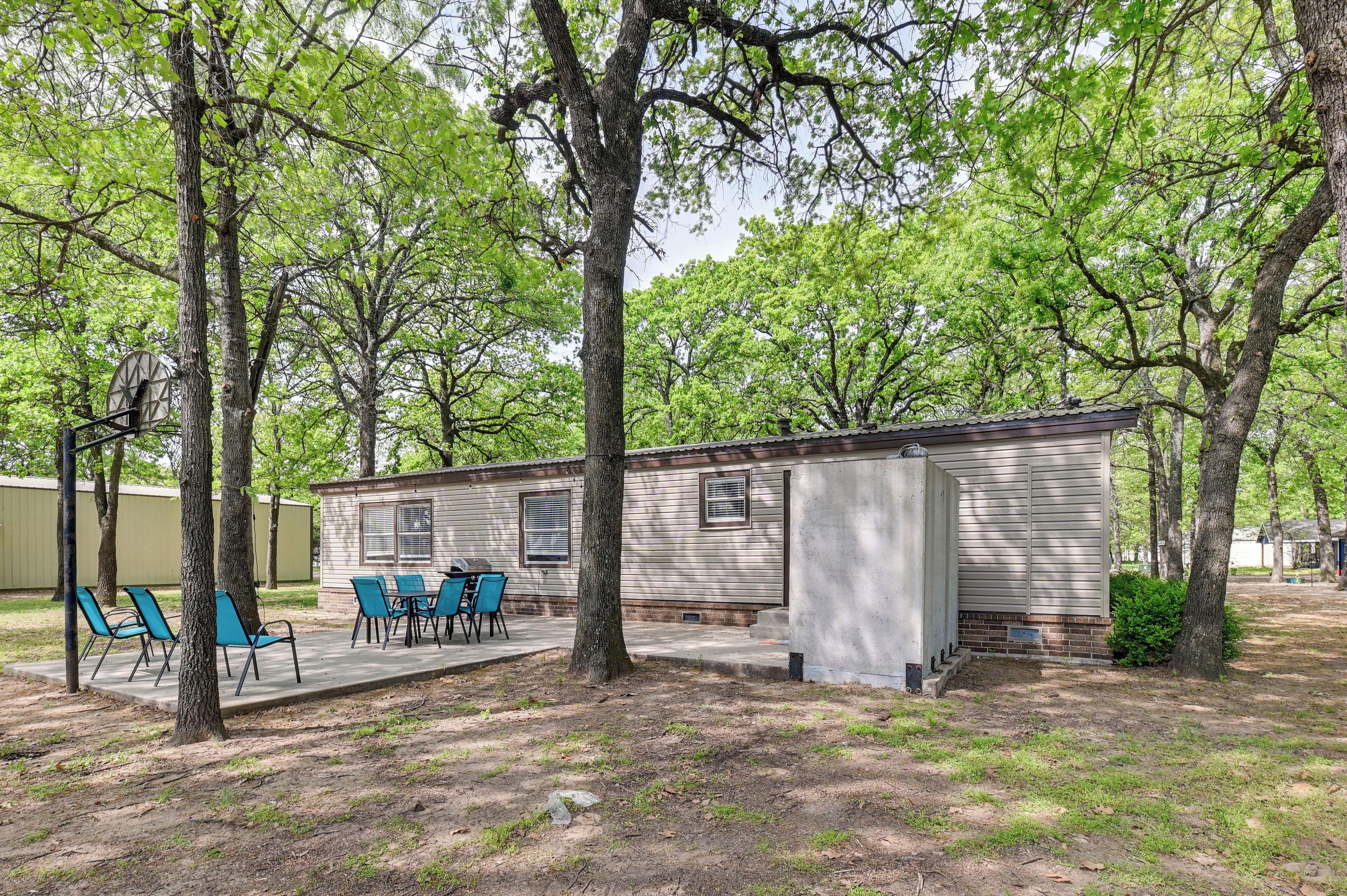 A small, single-story mobile home with a patio area featuring blue chairs and a table.