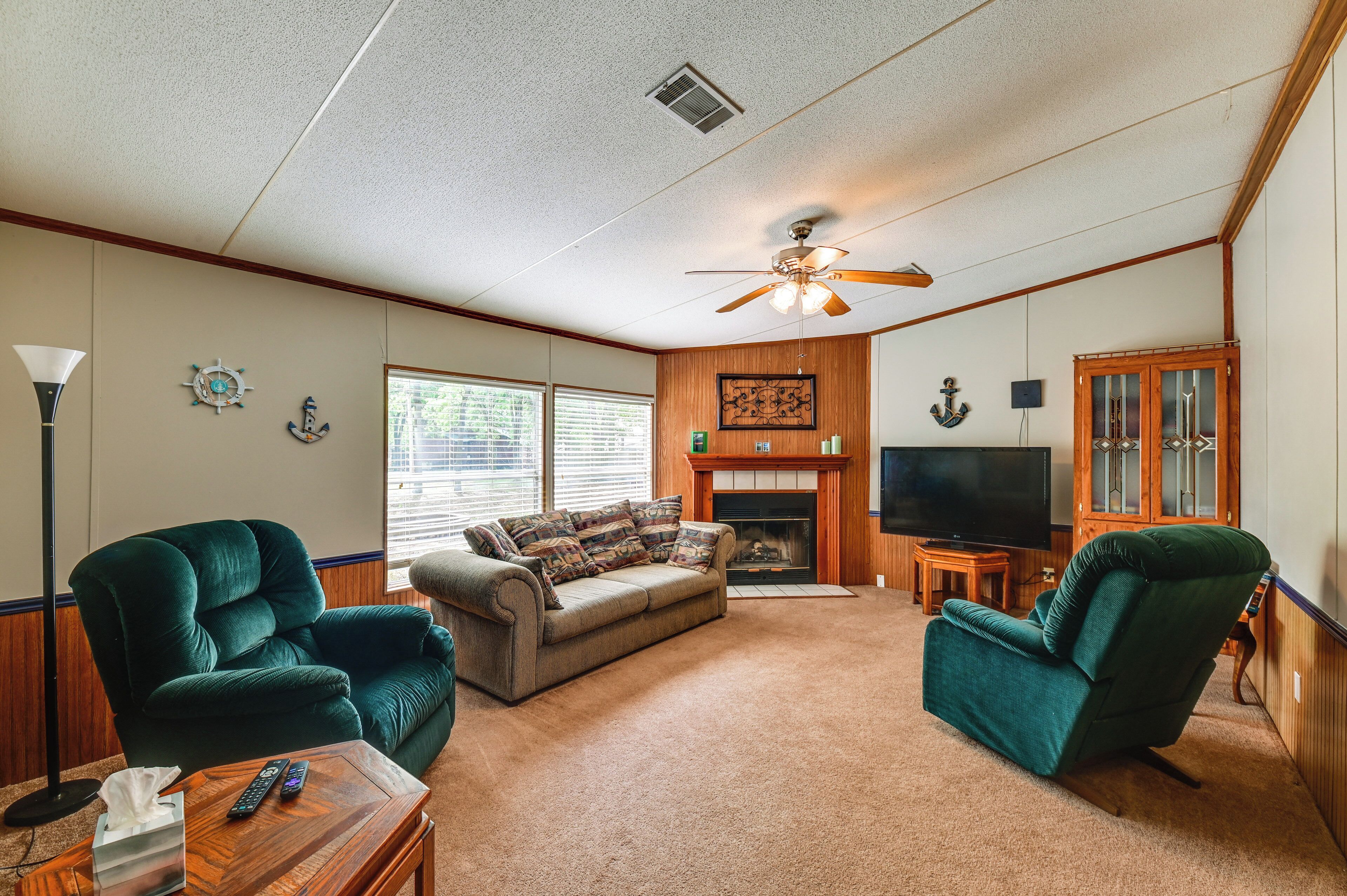 A living room with a fireplace, a ceiling fan, a television, and two green armchairs.