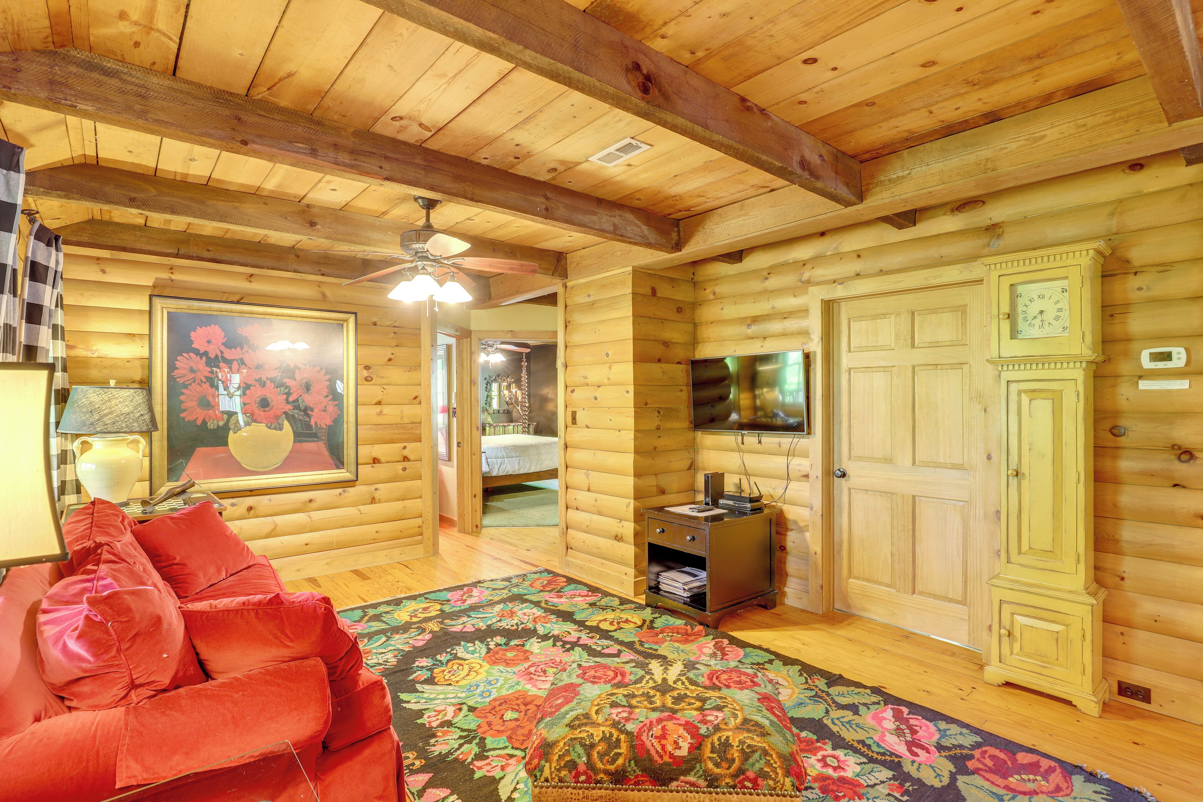 Un dormitorio tipo cabaña de troncos con cama, un sofá rojo, techo de madera y televisor en la pared.