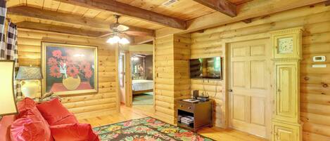 Un dormitorio tipo cabaña de troncos con cama, un sofá rojo, techo de madera y televisor en la pared.