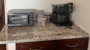Une cuisine équipée d’un grille-pain, d’une machine à café, d’un bocal de collations et d’un tableau encadré accroché au mur.