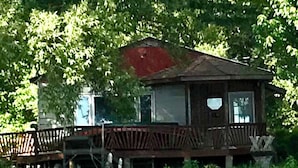 Une cabane en bois avec un toit rouge, une terrasse et un petit porche.