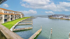 Een hotel aan het water met meerdere balkons, een steiger die in het water uitsteekt en een helder uitzicht op de zee.