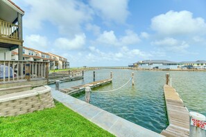 A waterfront property with a dock extending into a calm body of water, a grassy area, and a building with a balcony. - Fish & Swim: Waterfront Rockport Condo w/ Views! (Rockport)