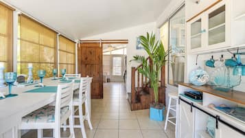 Una cocina amplia con comedor, que cuenta con una isla grande, armarios blancos y una planta en maceta.
