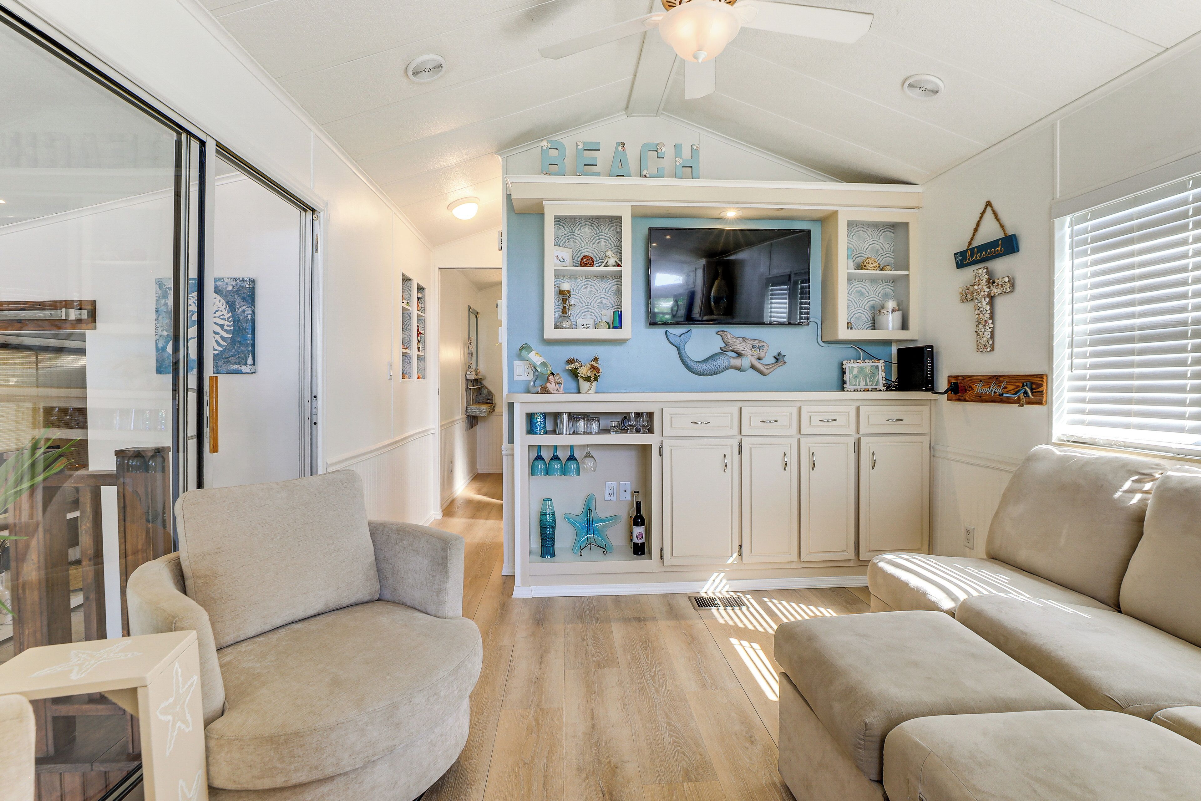 Un salón decorado con motivos playeros, con una televisión, estanterías con adornos y dos sofás color beige.