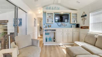 Un salón decorado con motivos playeros, con una televisión, estanterías con adornos y dos sofás color beige.