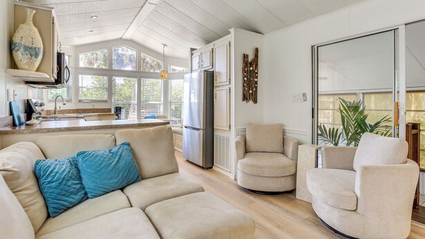 Eine moderne Küche mit einer großen Kochinsel, einem Einbauofen und einem Kühlschrank. Es gibt ein beiges Sofa mit blauen Kissen und einen beigen Sessel.