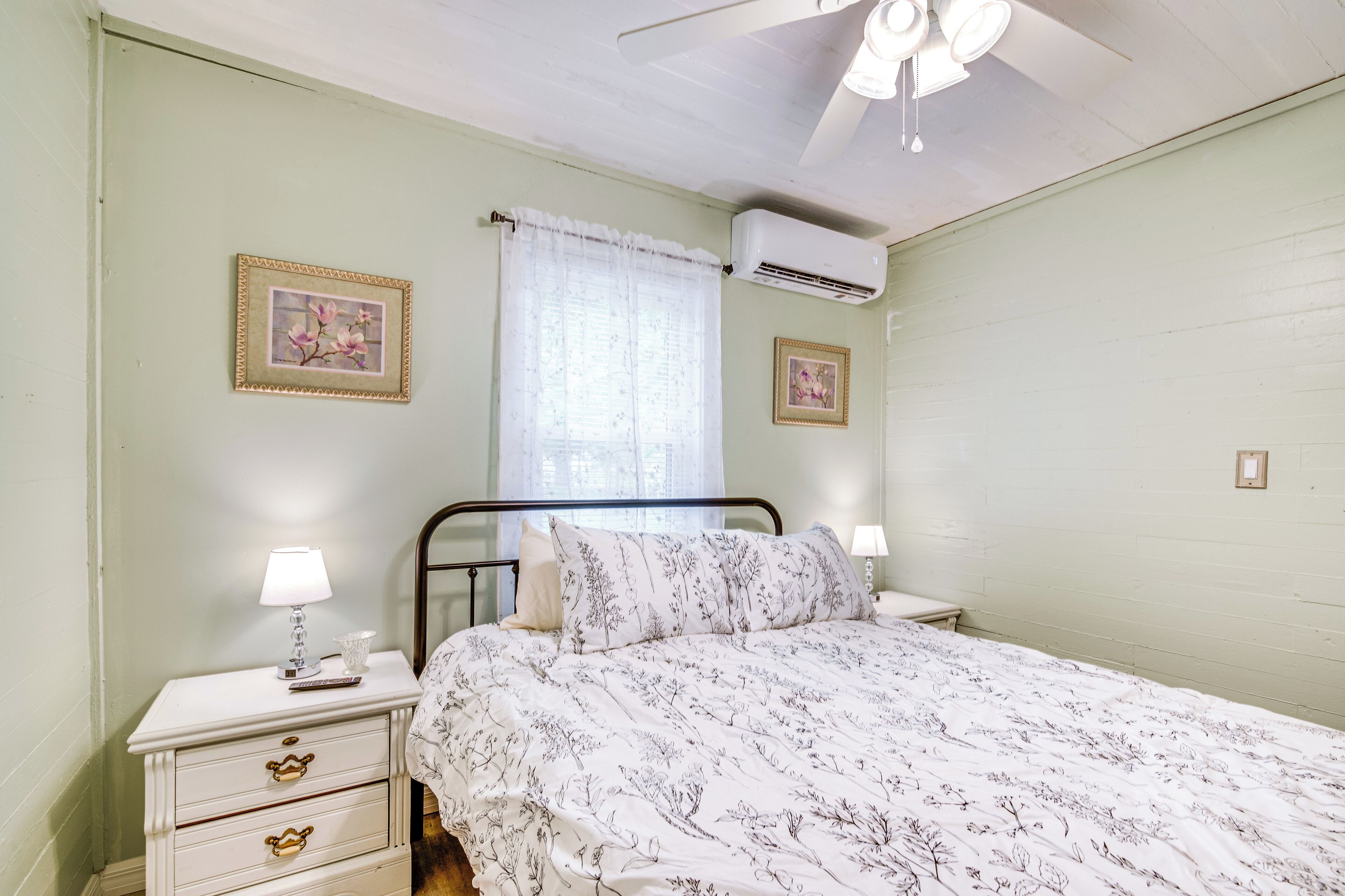 Un dormitorio con cama, mesitas de noche, ventilador de techo y aire acondicionado instalado en la pared.