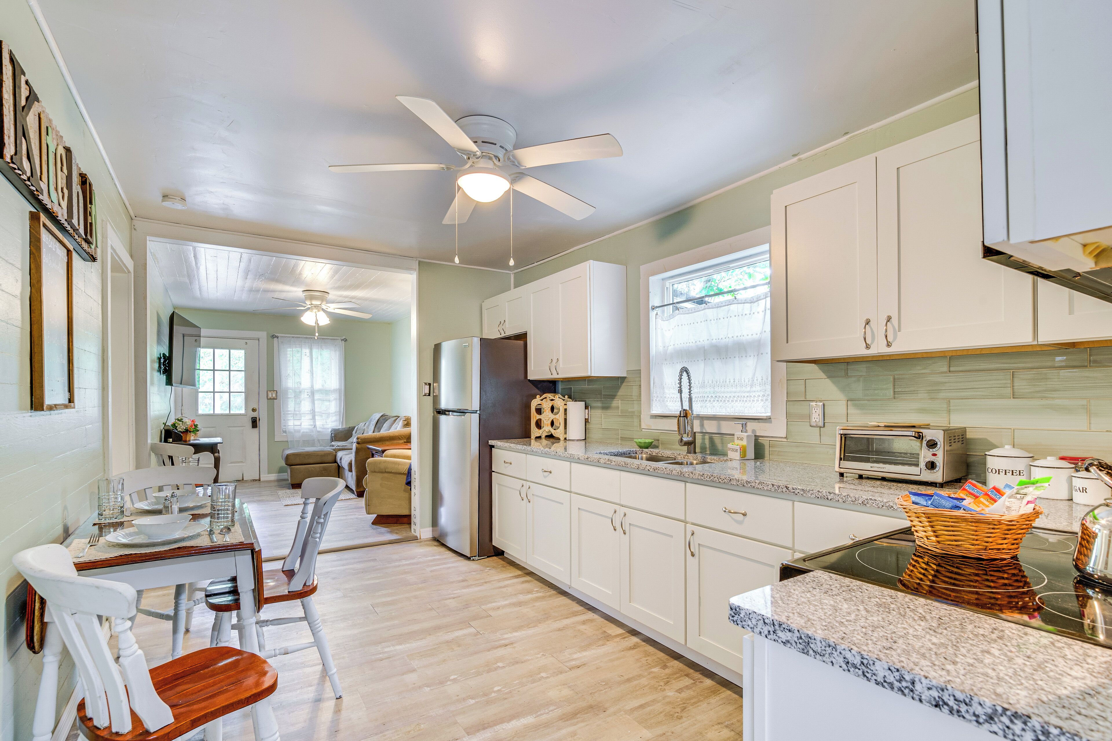 A spacious kitchen with white cabinets, a granite countertop, a built-in oven, and a ceiling fan.