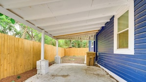 A covered patio area with a wooden fence, a concrete floor, and a blue house in the background. - 1 Mi to Ocala Dtwn Square: Home w/ Yard! (Ocala)