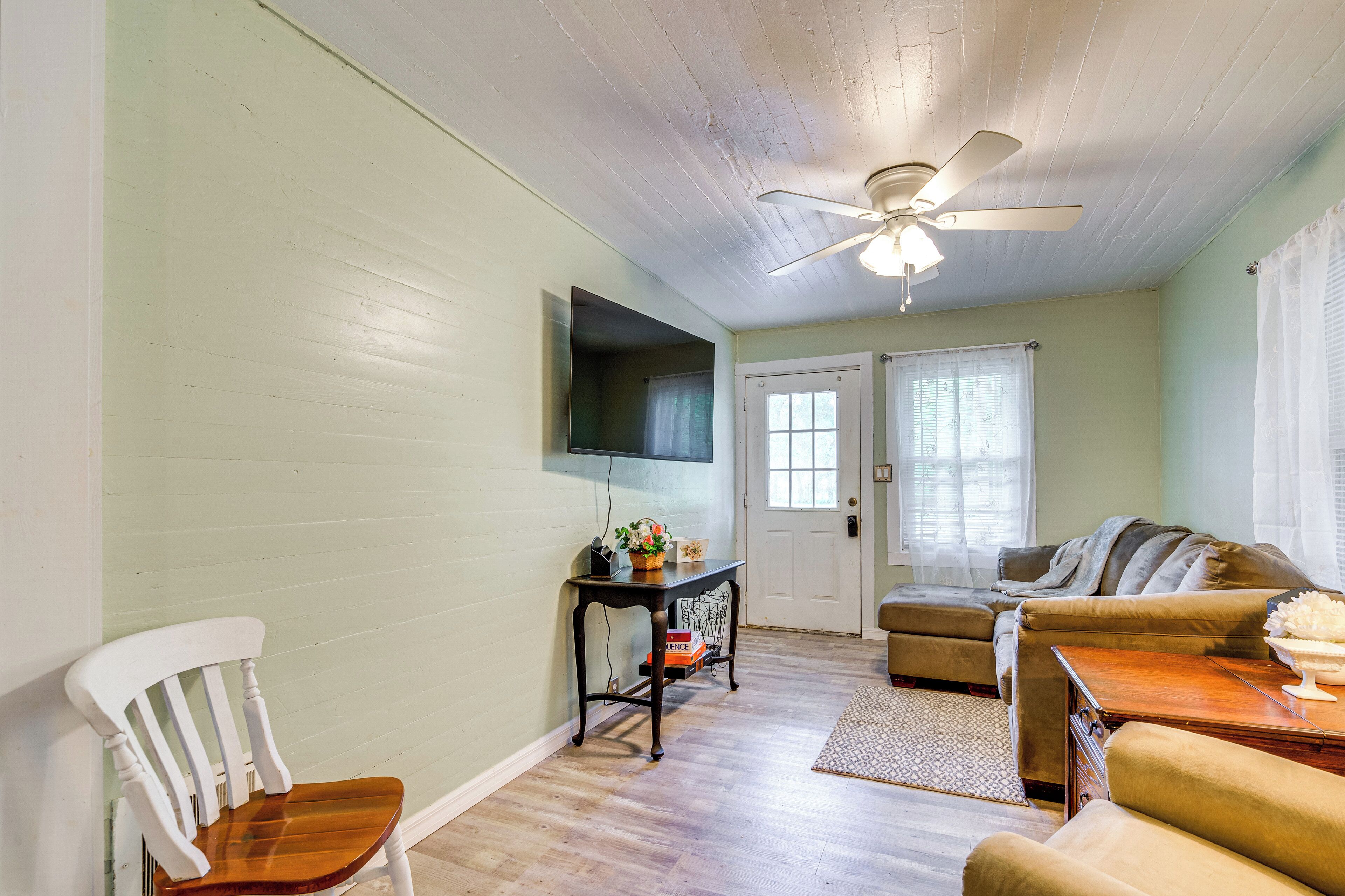 A living room with a ceiling fan, a television mounted on the wall, a sofa, a chair, and a small table with a bowl.