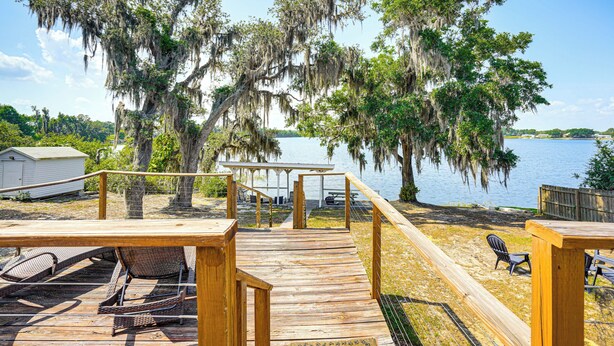 A wooden deck with a view of a lake, surrounded by trees with Spanish moss.