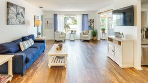 A spacious living room with a blue sofa, a coffee table, and a TV mounted on the wall.