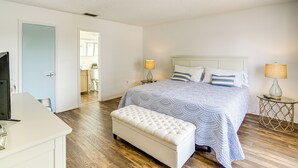 A bedroom with a bed, bedside lamps, a bench, and a desk.