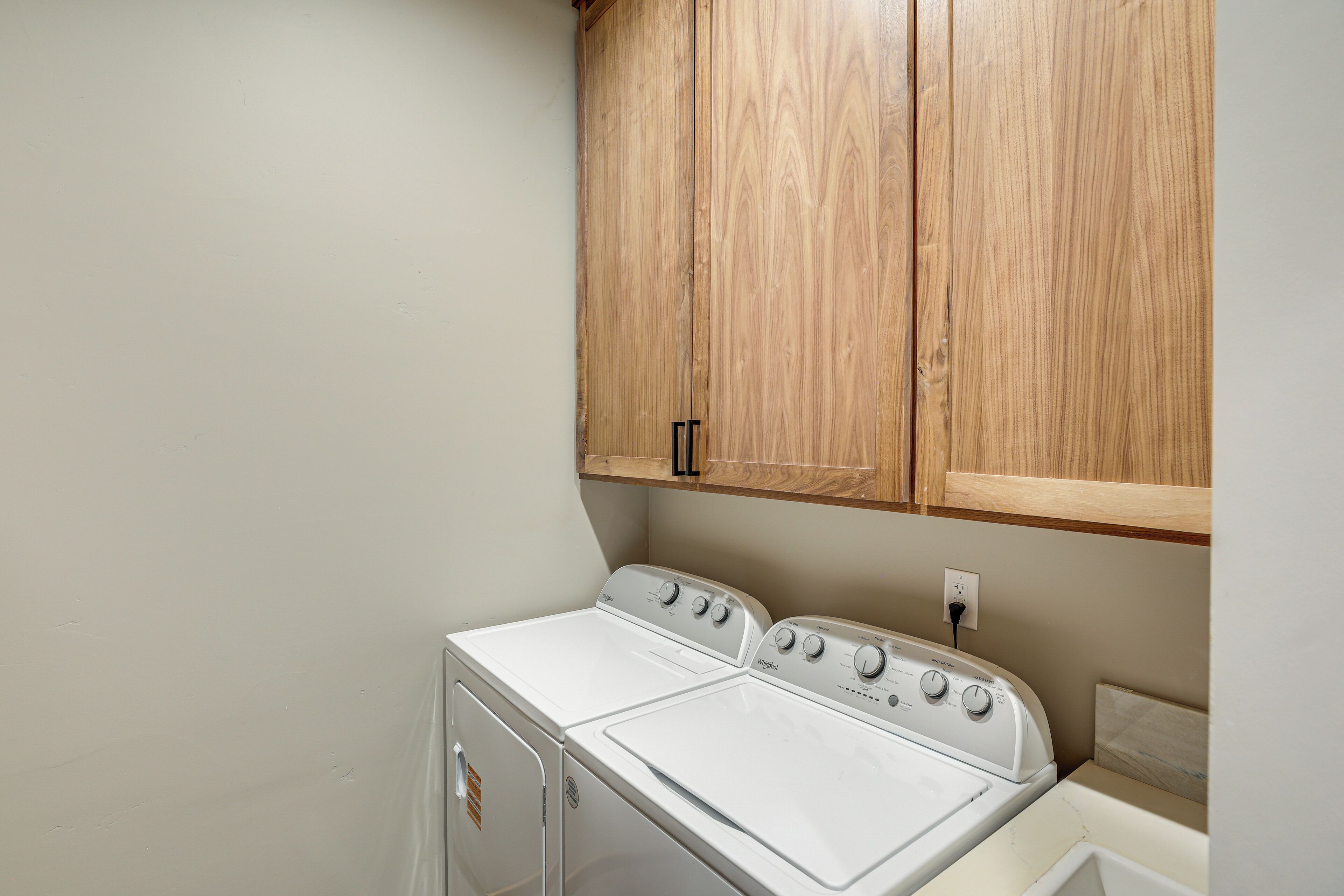 A laundry room with a front-loading washer and dryer, wooden cabinets above, and a white countertop.